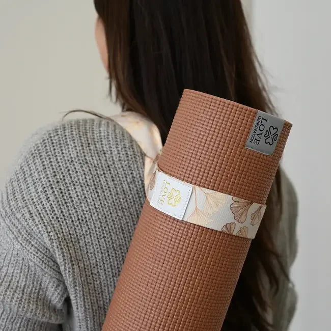 Vrouw draagt een bruine yogamat met bloemen draagriem over schouder, mindful yoga accessoire