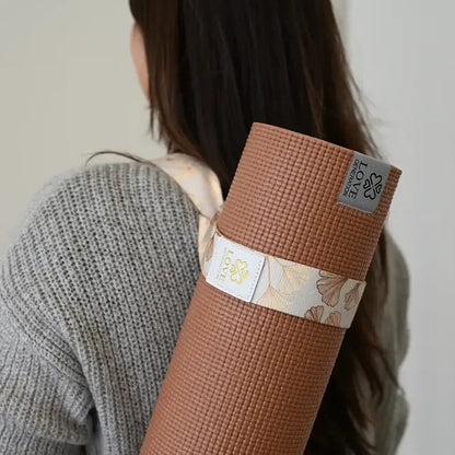 Vrouw draagt een bruine yogamat met bloemen draagriem over schouder, mindful yoga accessoire