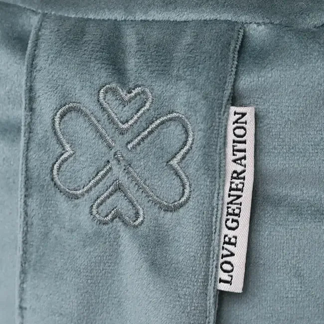 Detail van zacht groen meditatiekussen met geborduurd klaverblad en label met tekst.