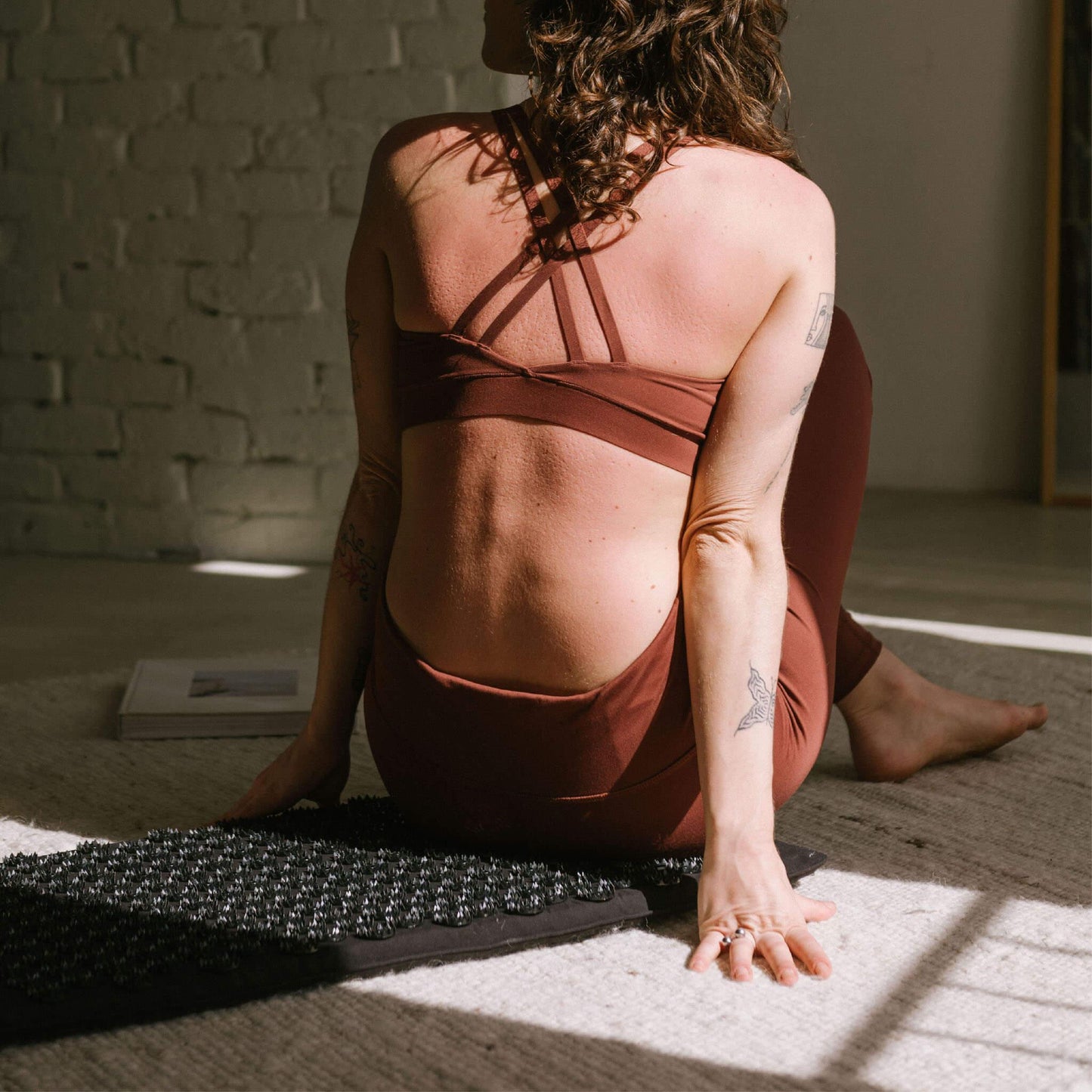 Vrouw in yoga-outfit op acupressuurmat voor ontspanning en zelfzorg, met zachte lichtval en rustige sfeer.