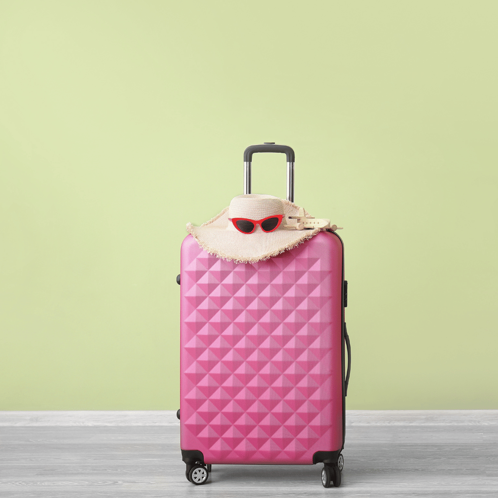 Roze koffertje met strooien hoed en rode zonnebril, perfect voor een zen reis of zelfzorgvakantie