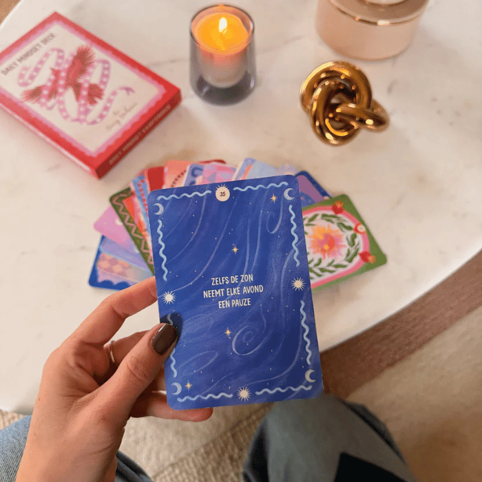 Blauwe zelfzorgkaart met sterren en tekst 'Zelfs de zon neemt elke avond een pauze', omringd door kaarten, kaars en decoratie