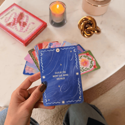 Blauwe zelfzorgkaart met sterren en tekst 'Zelfs de zon neemt elke avond een pauze', omringd door kaarten, kaars en decoratie