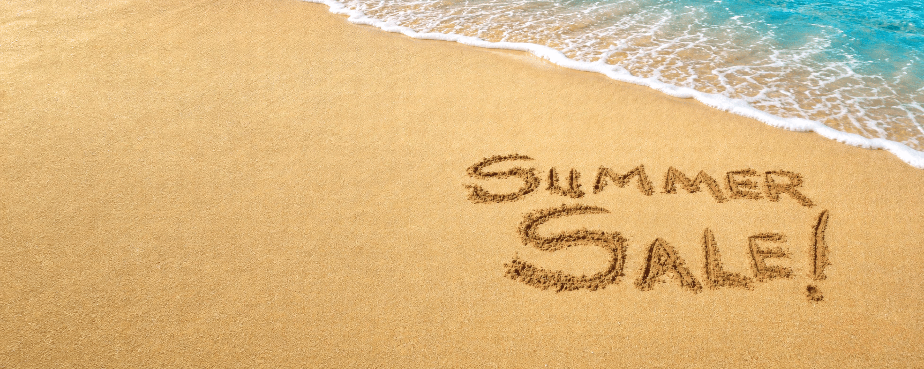 Summer Sale geschreven in het zand bij het strand, met golven erbij