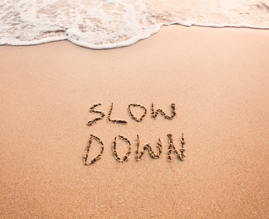 ‘Slow Down’ geschreven in zand bij golven — rust, mindfulness, zelfzorg en ontspanning